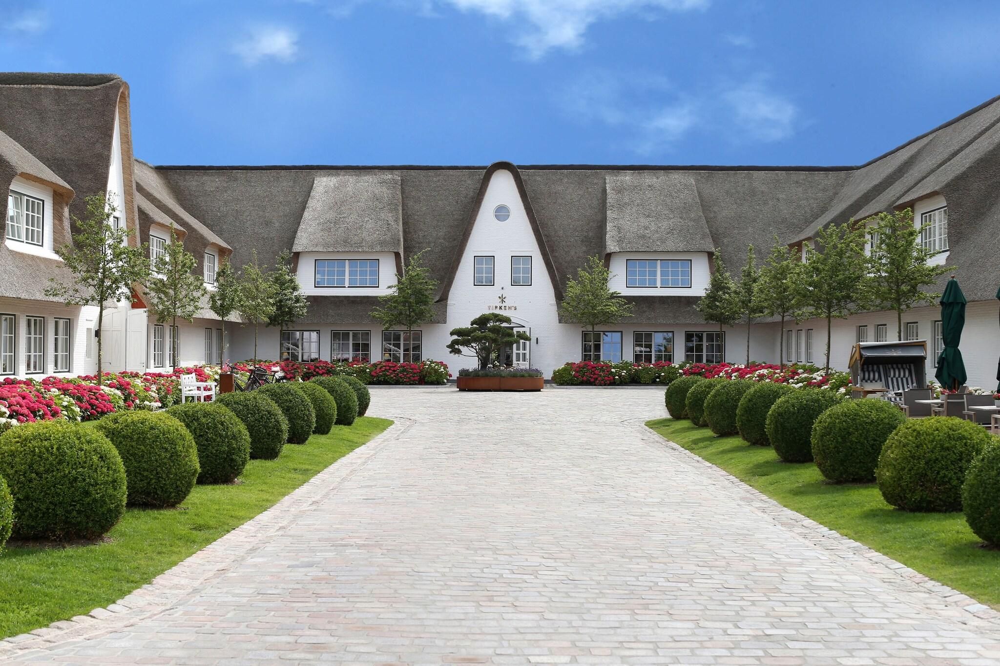 A courtyard with a central pathway leading to a building with a thatched roof.