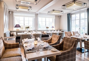 A dining area with multiple tables and chairs, large windows, and modern ceiling lights. - Severin's Resort & Spa (Sylt)
