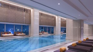 A modern indoor swimming pool with seating areas and city views.