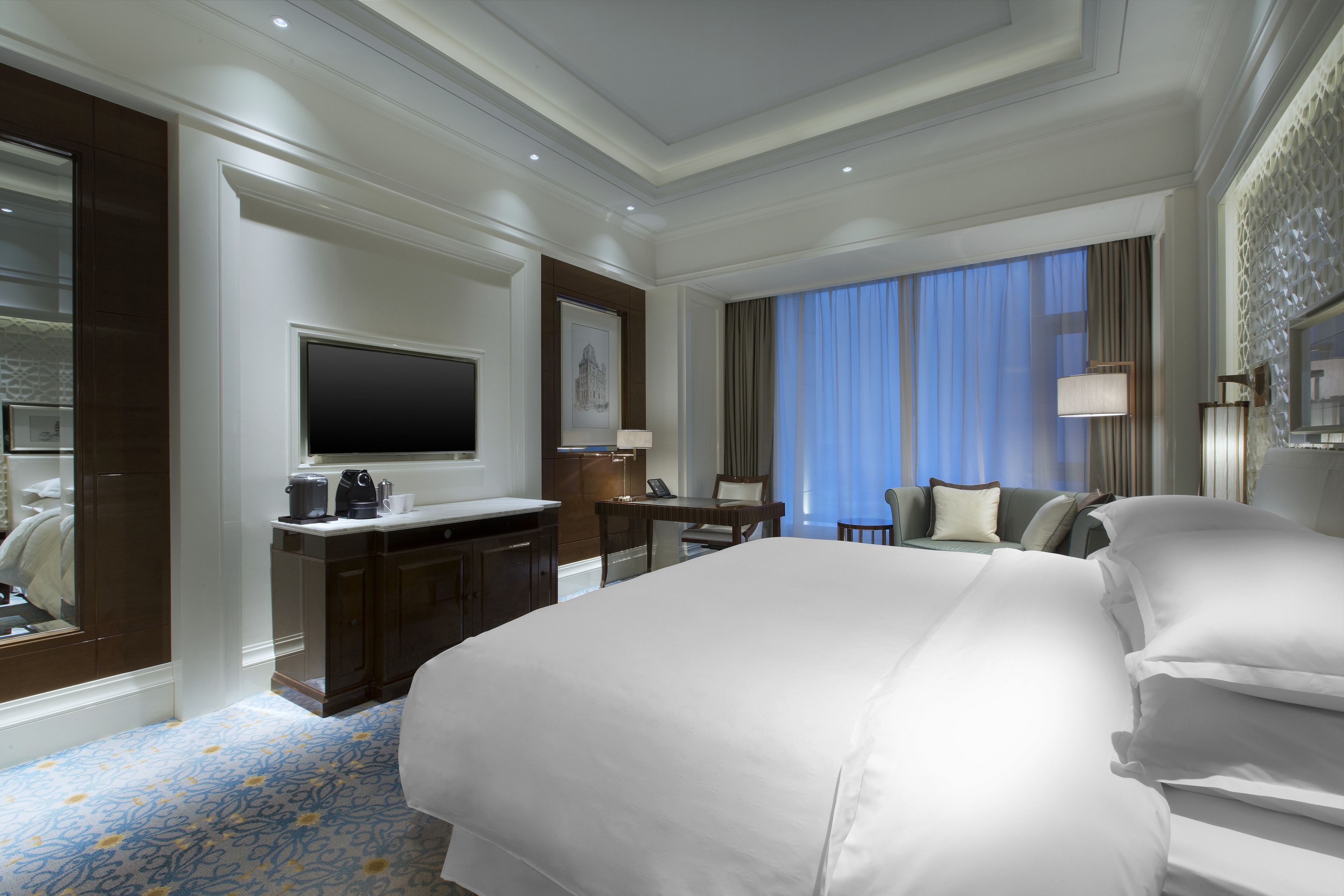 Una habitación de hotel con una cama grande, un escritorio con computadora, un televisor y una zona de estar con sofá y sillas.