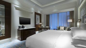 Una habitación de hotel con una cama grande, un escritorio con computadora, un televisor y una zona de estar con sofá y sillas.