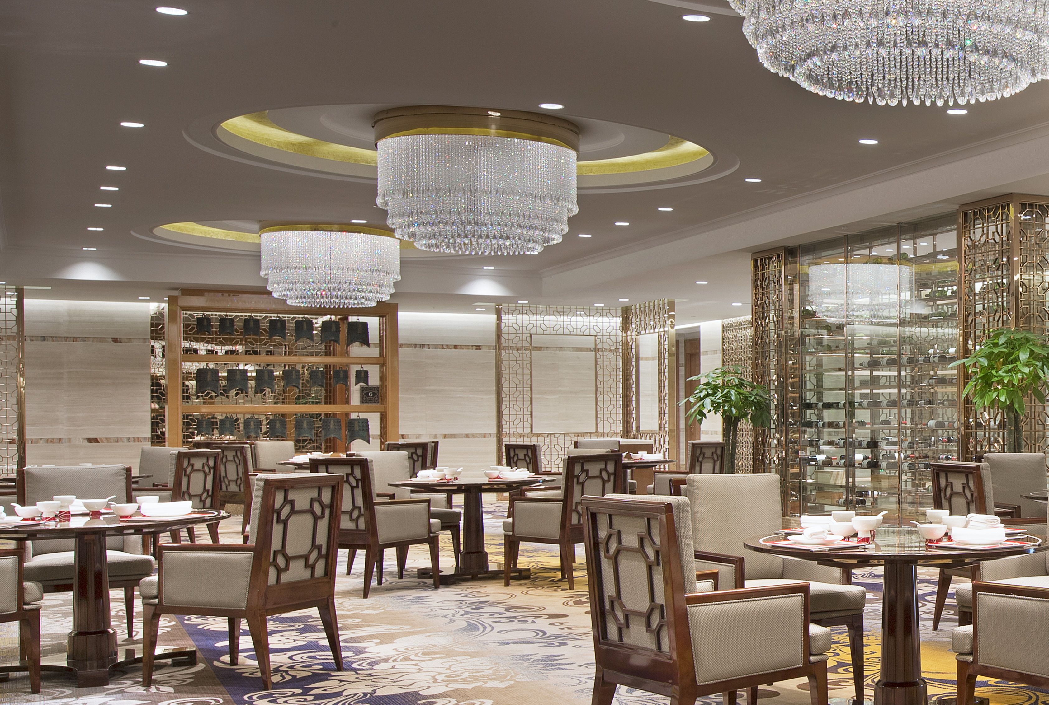 A luxurious dining area with chandeliers, wooden furniture, and a decorative glass partition.