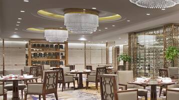 Un comedor lujoso con candelabros, muebles de madera y un separador decorativo de vidrio.