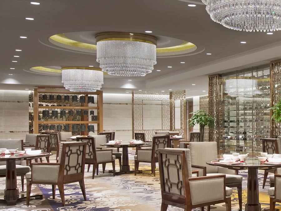 Un comedor lujoso con candelabros, muebles de madera y un separador decorativo de vidrio.