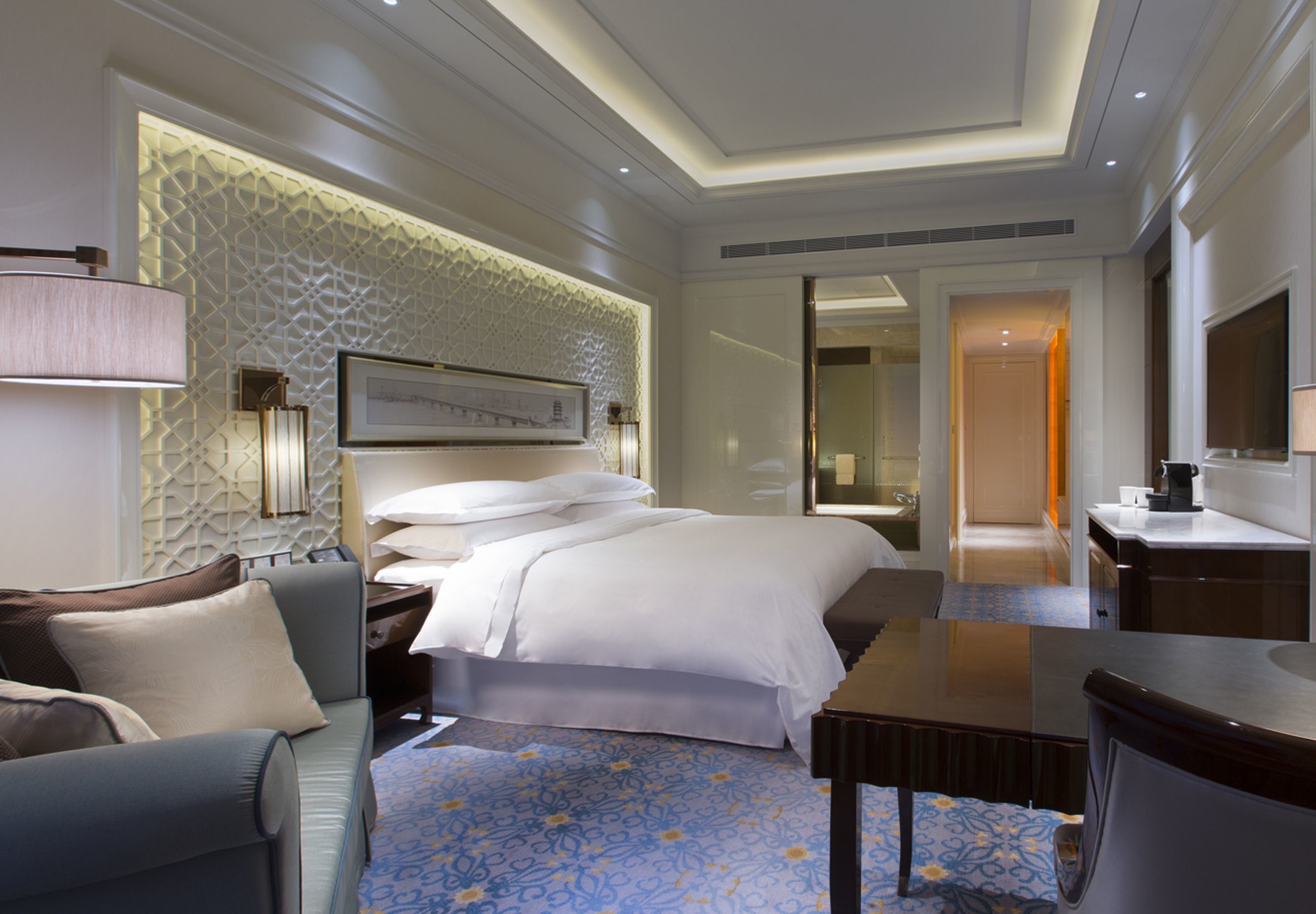 A hotel room with a bed, a sofa, a desk, and a bathroom visible through an open door.