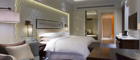 A hotel room with a bed, a sofa, a desk, and a bathroom visible through an open door.