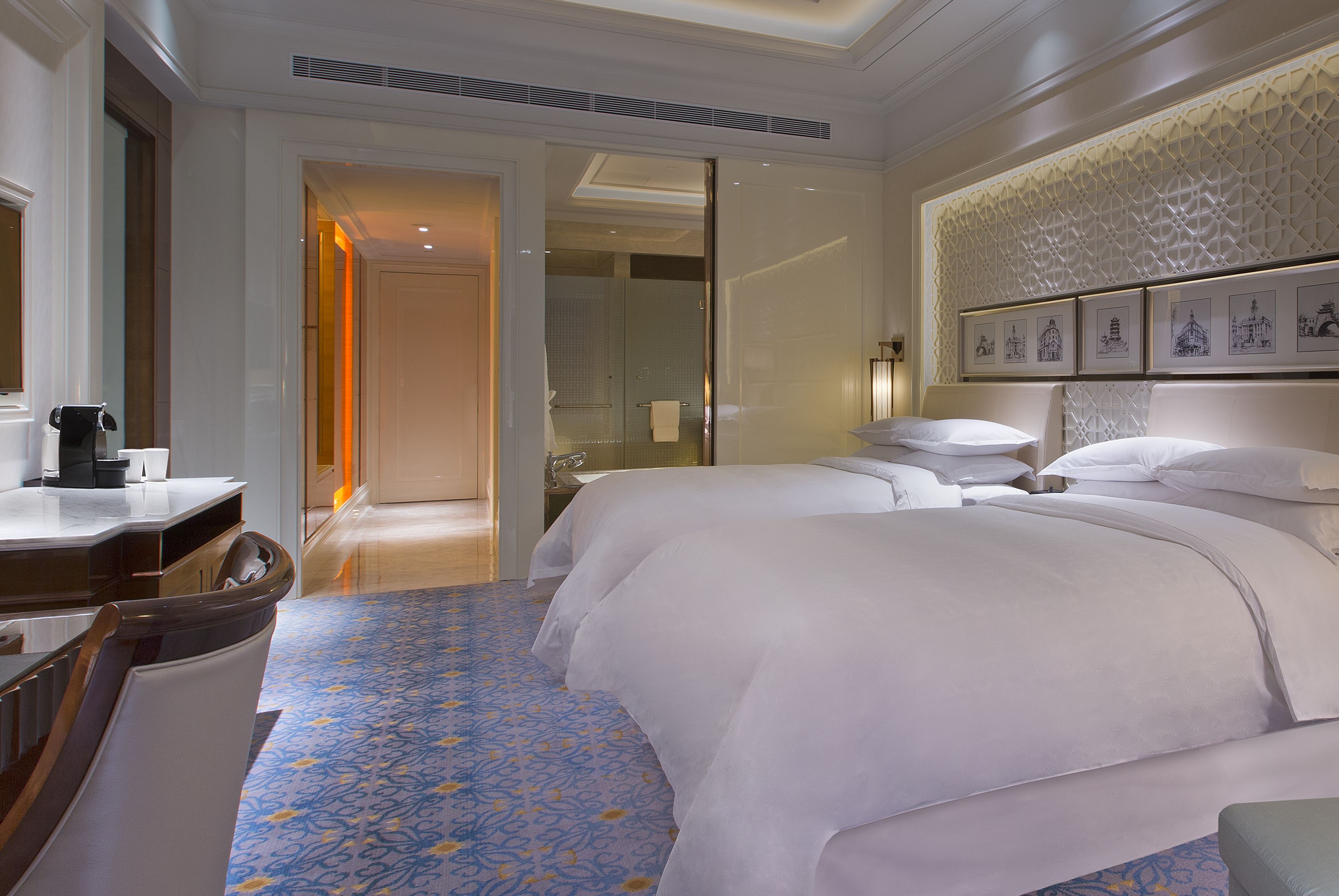 Habitación de hotel con una cama grande, un escritorio y un baño con ducha de vidrio.