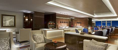 A modern hotel lobby with seating areas, a bar, and a view of the city.