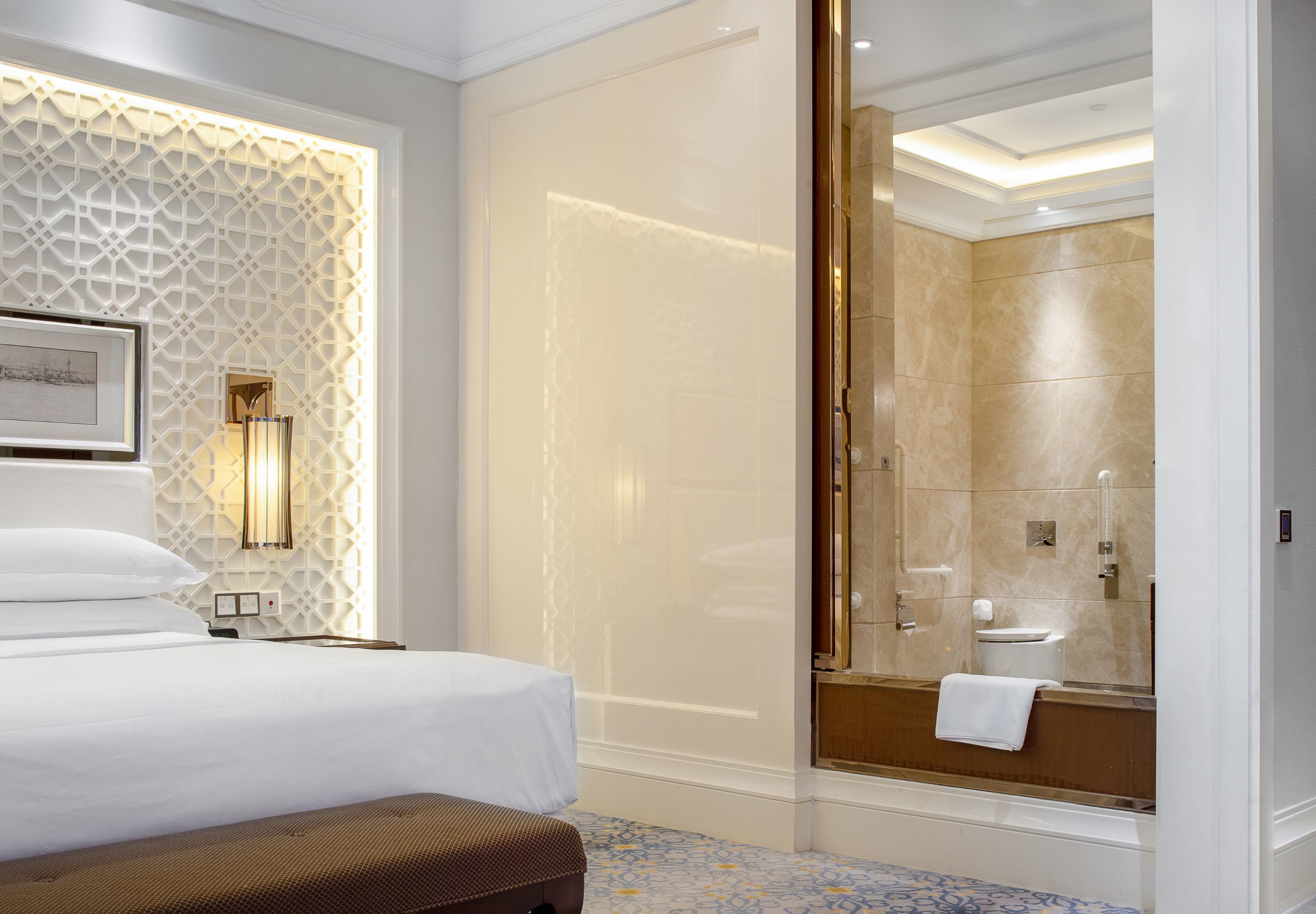 A hotel room with a bed, a large mirror, a shower area, and a patterned wall.