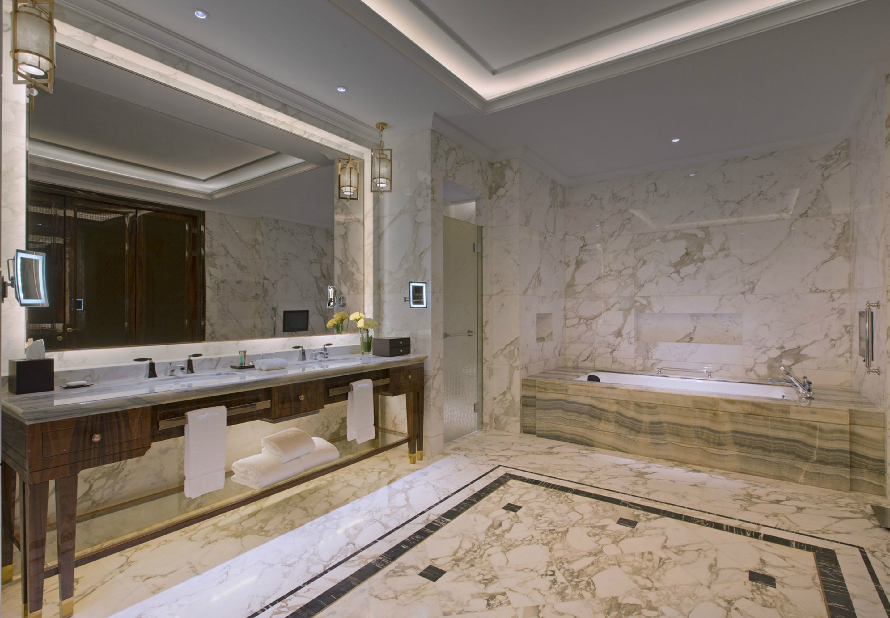 A luxurious bathroom with a marble vanity, a large mirror, a bathtub, and a marble floor.