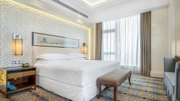 A hotel room with a large bed, a bedside table, a bench, a TV, and a patterned carpet.