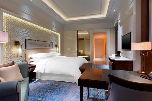 A hotel room with a large bed, a desk, a chair, a TV, and a bathroom visible through an open door. - Sheraton Grand Wuhan Hankou Hotel (Wuhan)