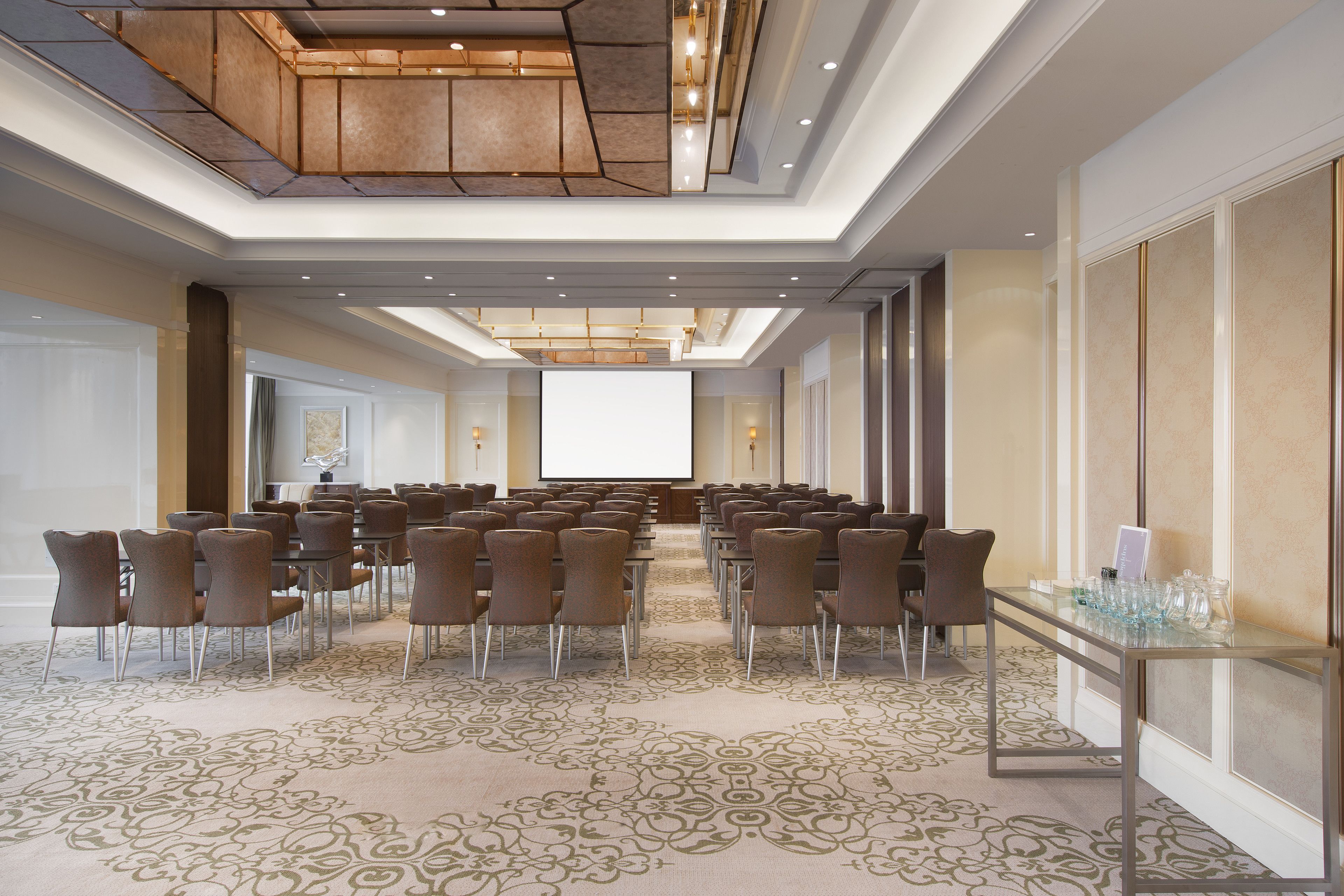A conference room with a long table and chairs, a carpeted floor, and a large screen at the front.