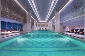 A large indoor swimming pool with a geometric tile pattern, lounge chairs, and seating areas with cushions. - Sheraton Grand Wuhan Hankou Hotel (Wuhan)
