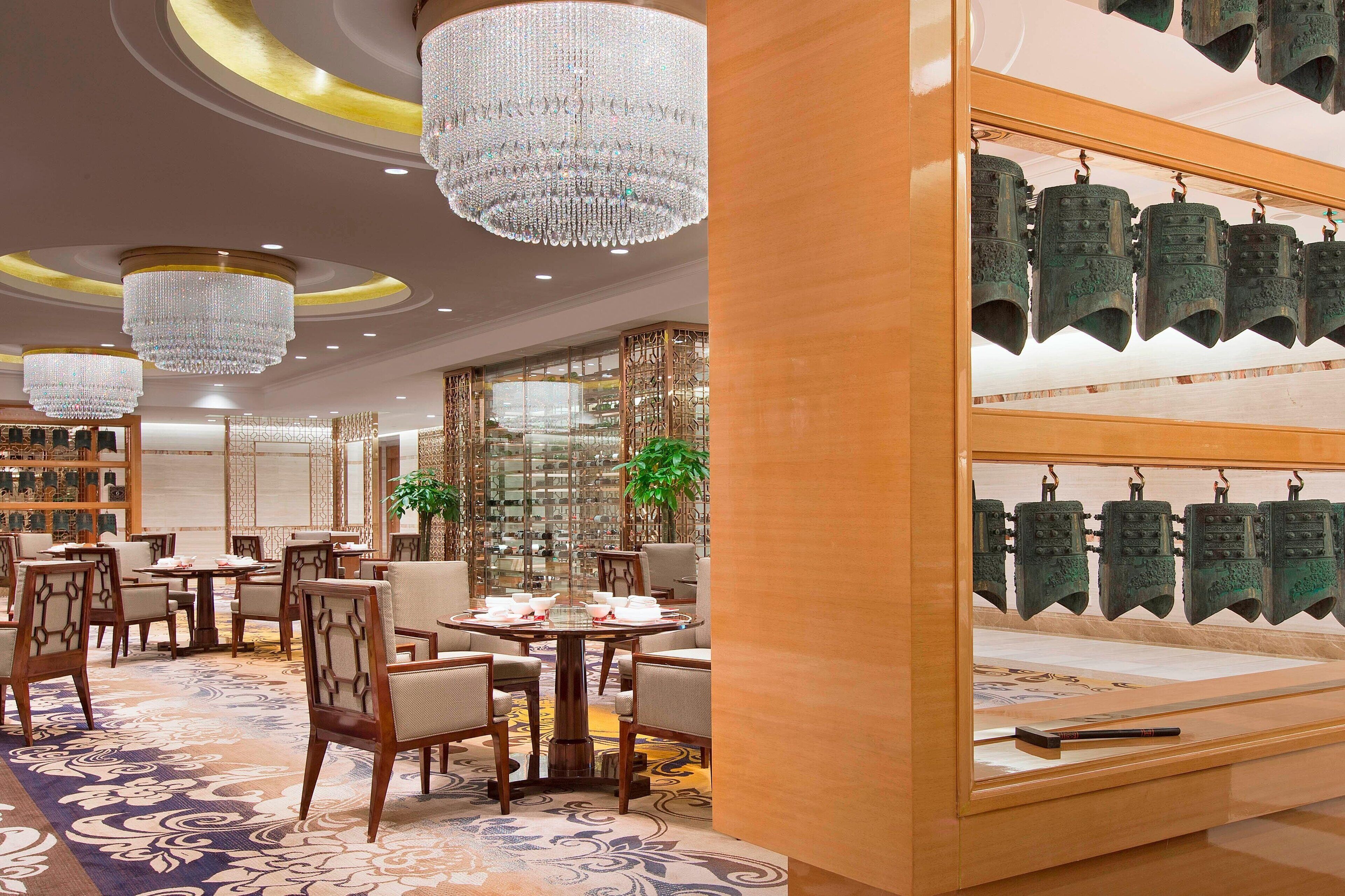 A luxurious hotel lobby with chandeliers, wooden furniture, and a display of traditional bells.