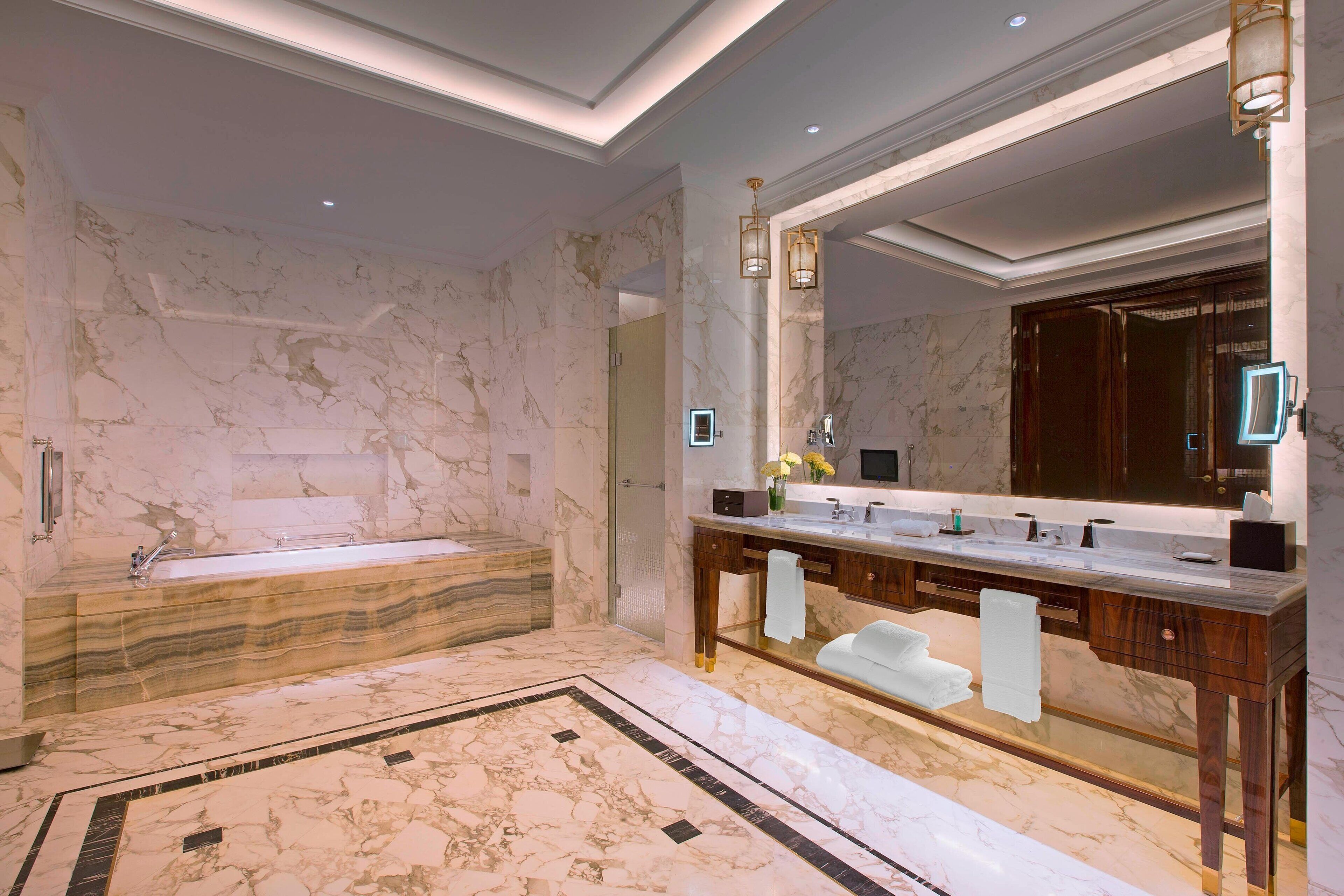 Ein luxuriöses Badezimmer mit Marmorboden, einer großzügigen Badewanne, einem Holzkosmetikschrank mit Spiegel und einer modernen Leuchte.