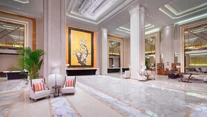 A spacious lobby with marble flooring, a large painting on the wall, and modern furniture.