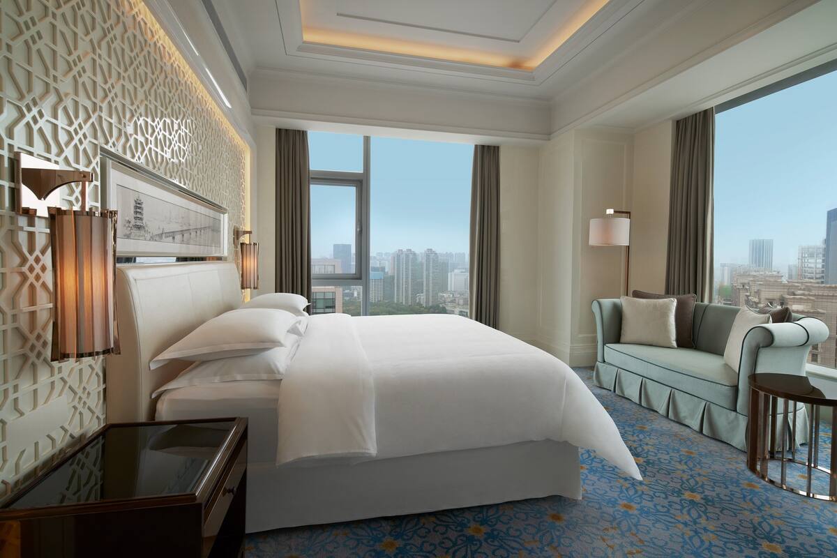 Een hotelkamer met een groot bed, een bank, een bureau en uitzicht op de stad.