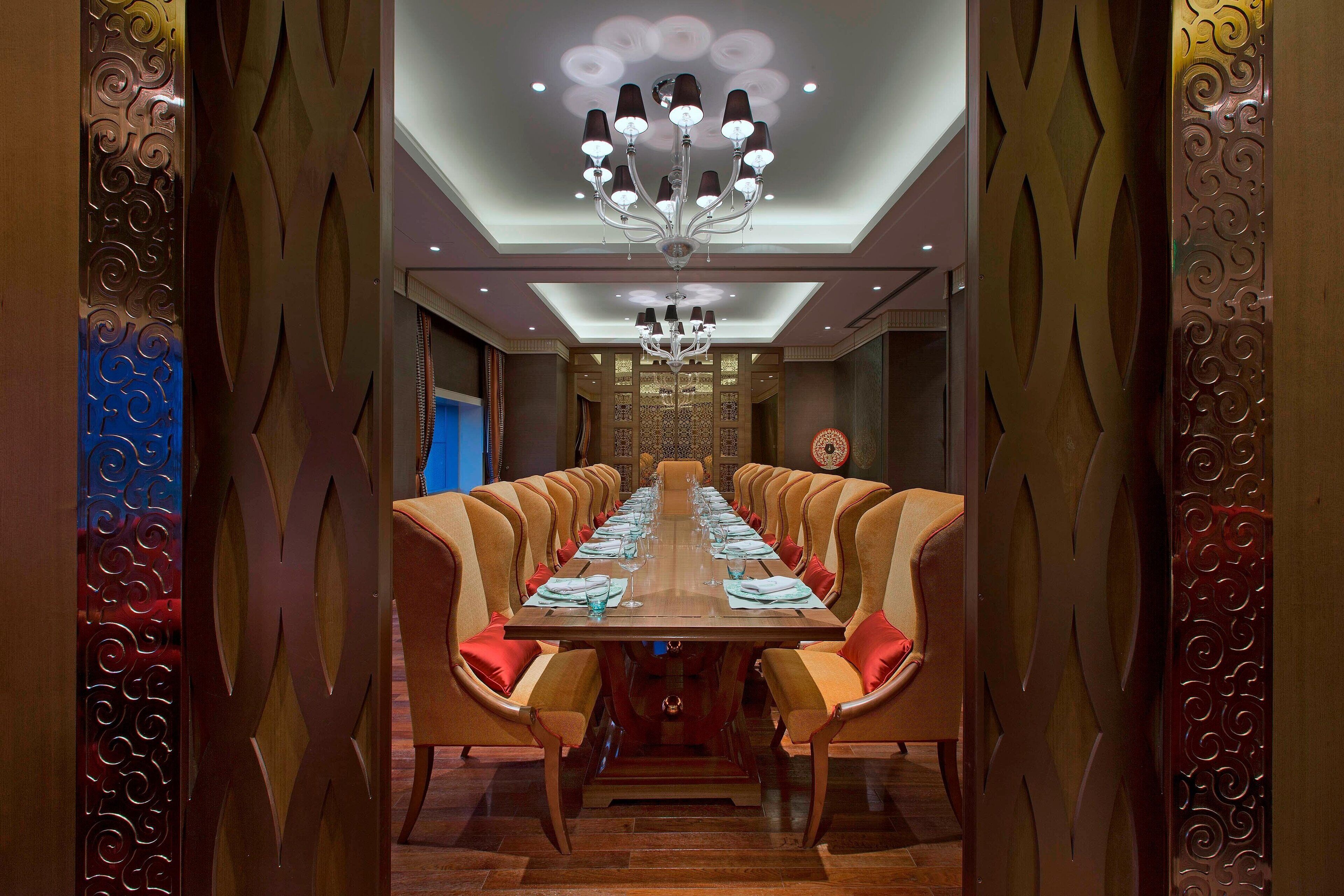 A long dining table with chairs, a chandelier, and decorative wall panels.
