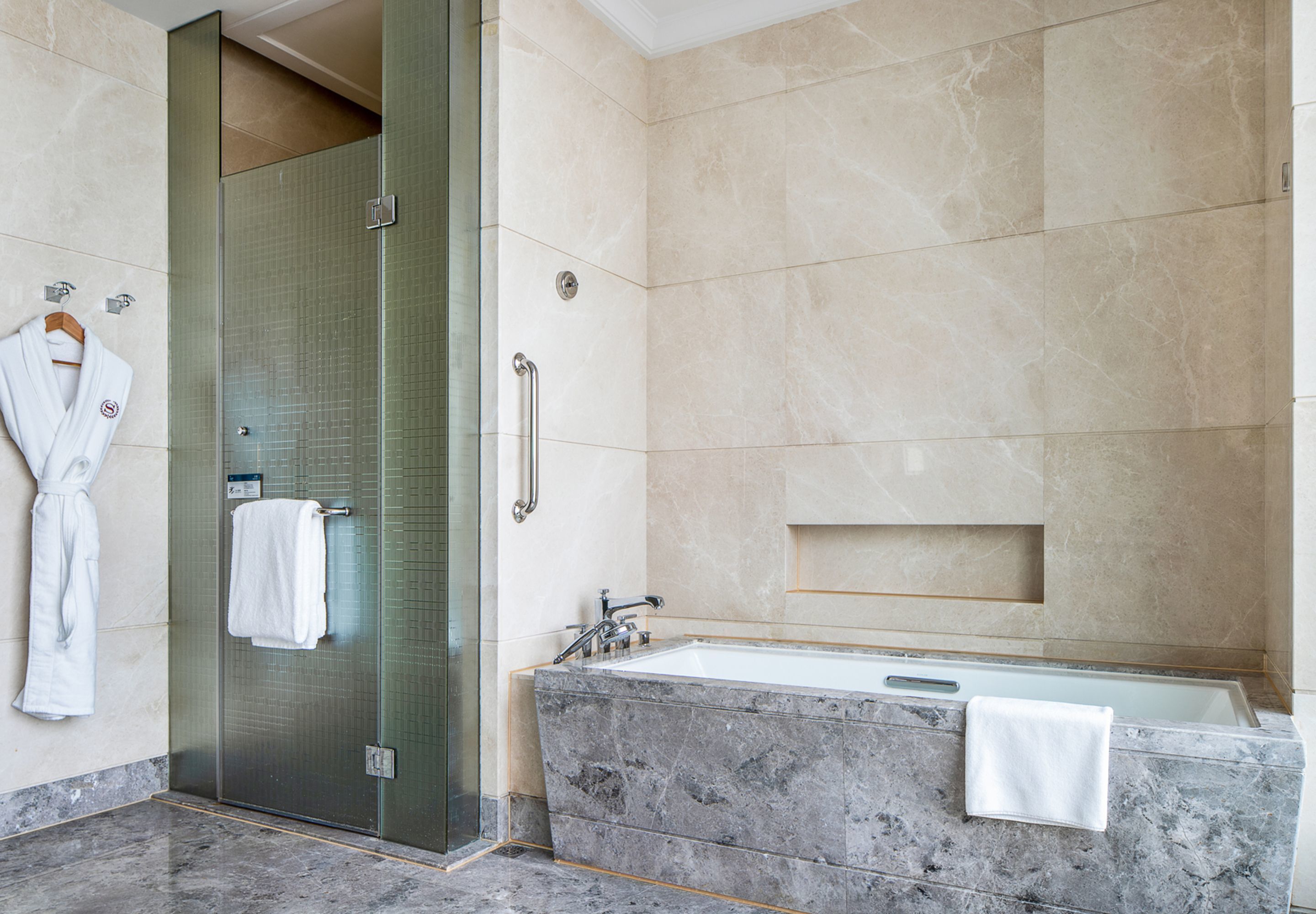 Un baño moderno con cabina de ducha de vidrio, una bañera de mármol y un perchero para toallas.