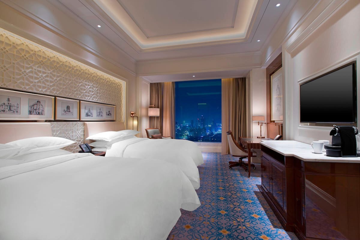 Een hotelkamer met twee bedden, een bureau met een koffiezetapparaat, een televisie en uitzicht op de stad.
