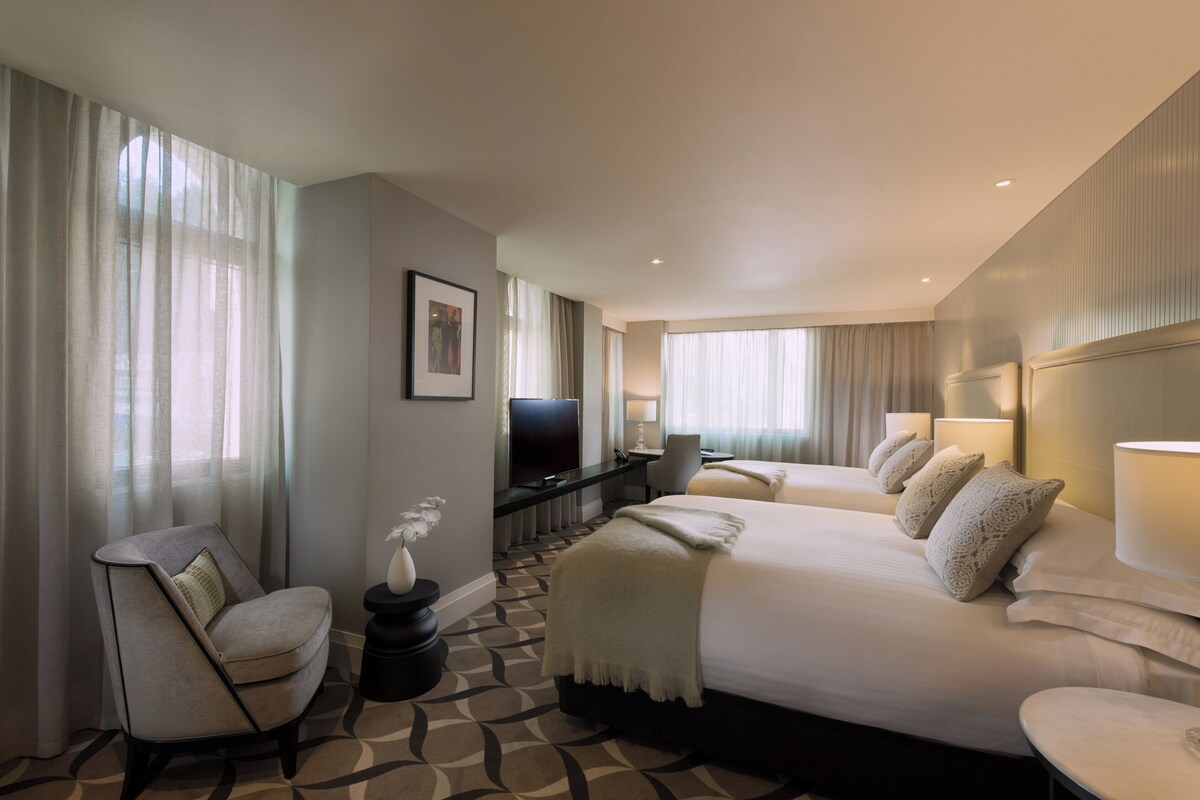 Une chambre d’hôtel avec deux lits, un bureau, une chaise et un téléviseur.