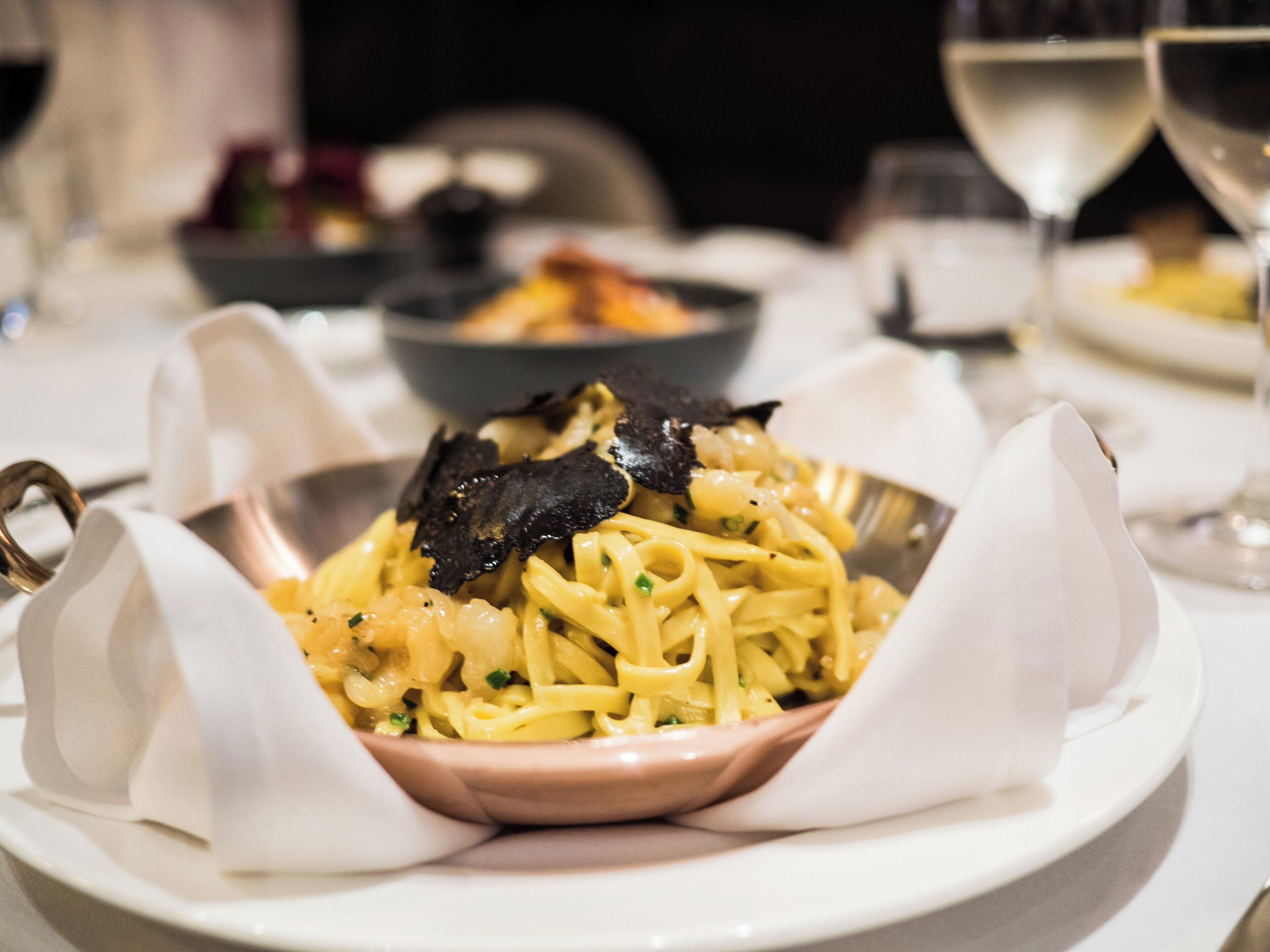 Un plato blanco con pasta, salsa cremosa y trufas negras.