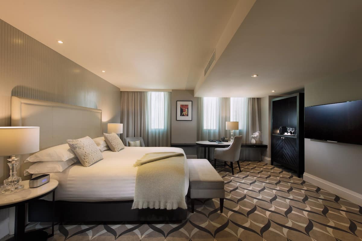 A hotel room with a large bed, bedside tables, a desk, a chair, a television, and a patterned carpet.
