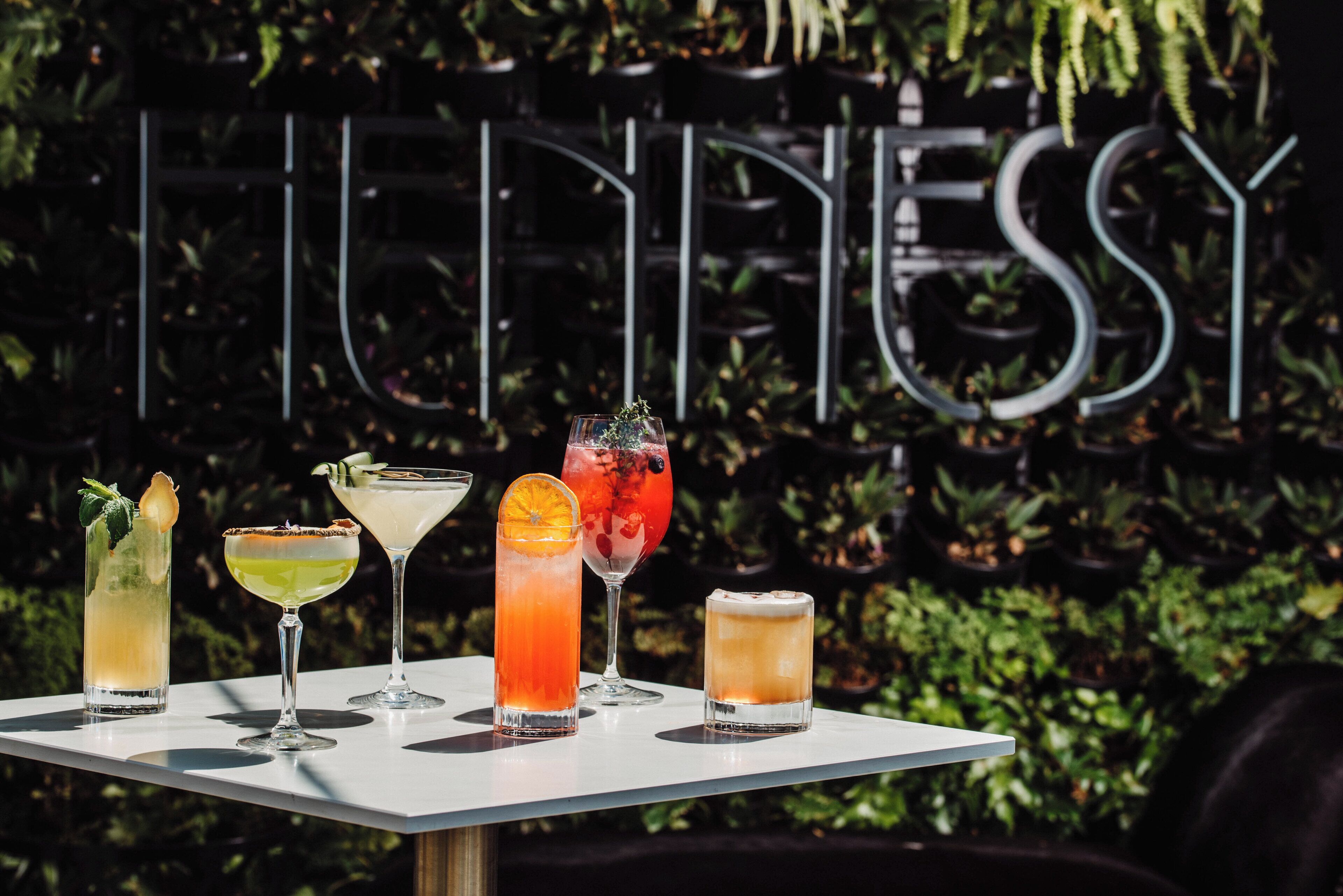 A table with five cocktails in front of a sign with the word "HENNESSY".
