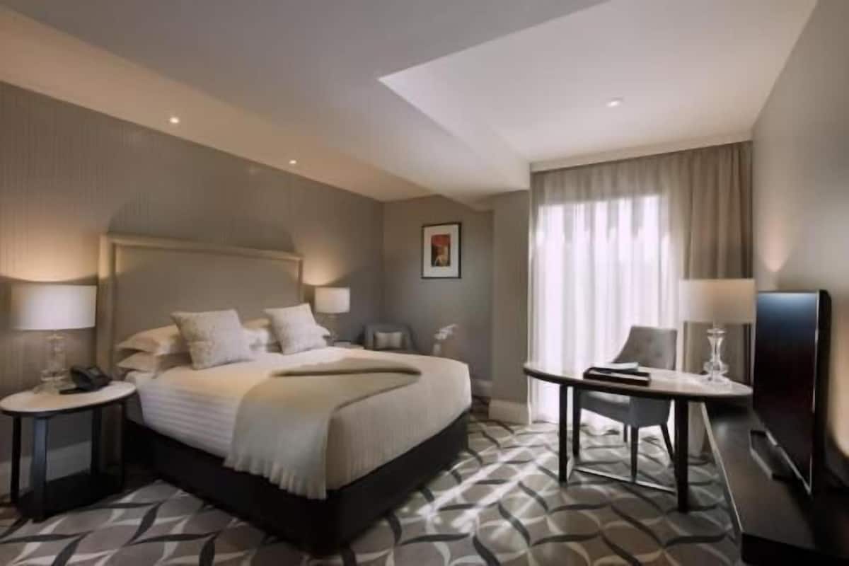 A hotel room with a large bed, bedside tables, a desk, and a television.