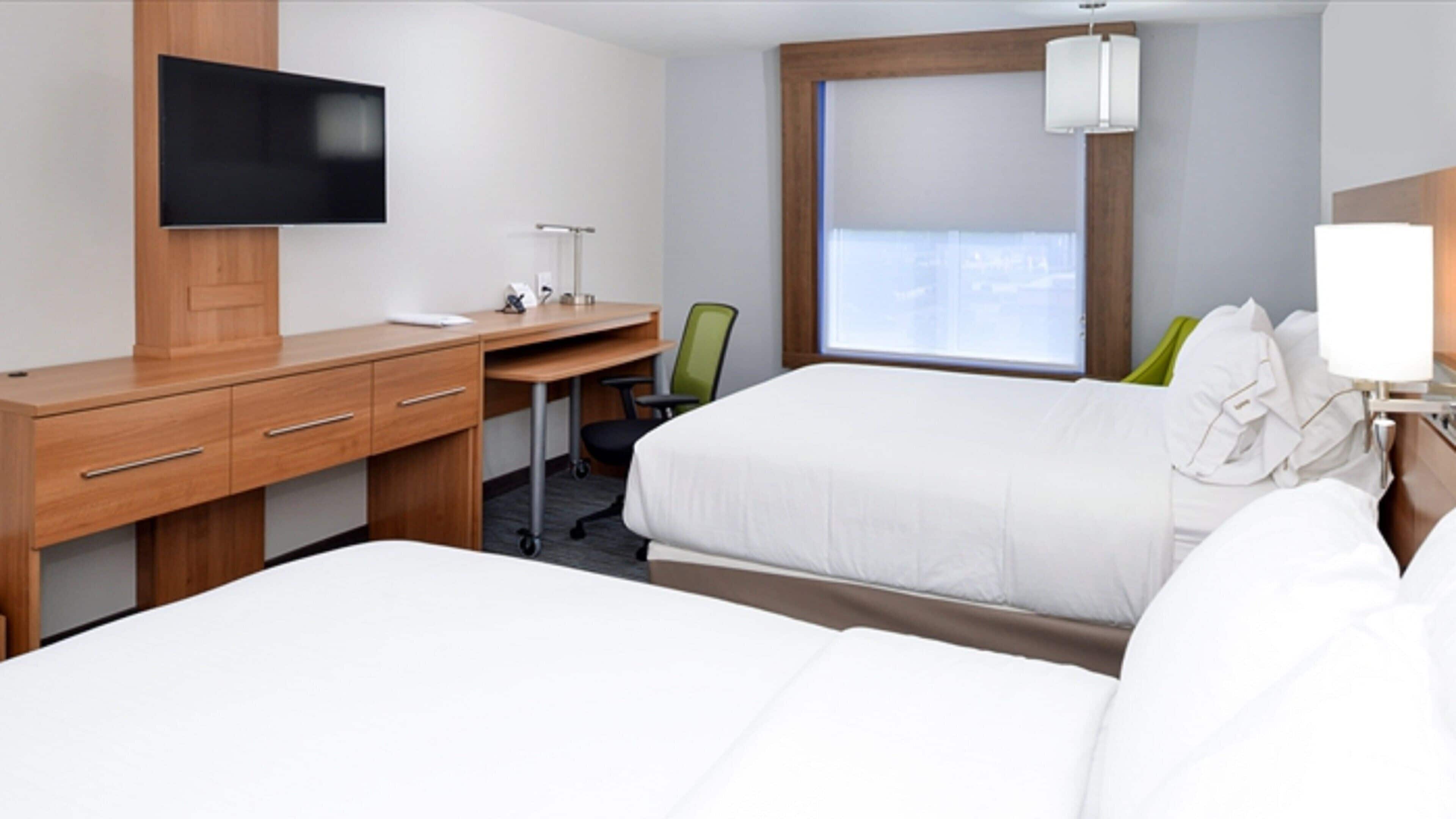 A hotel room with two beds, a desk, a chair, a TV, and a window.