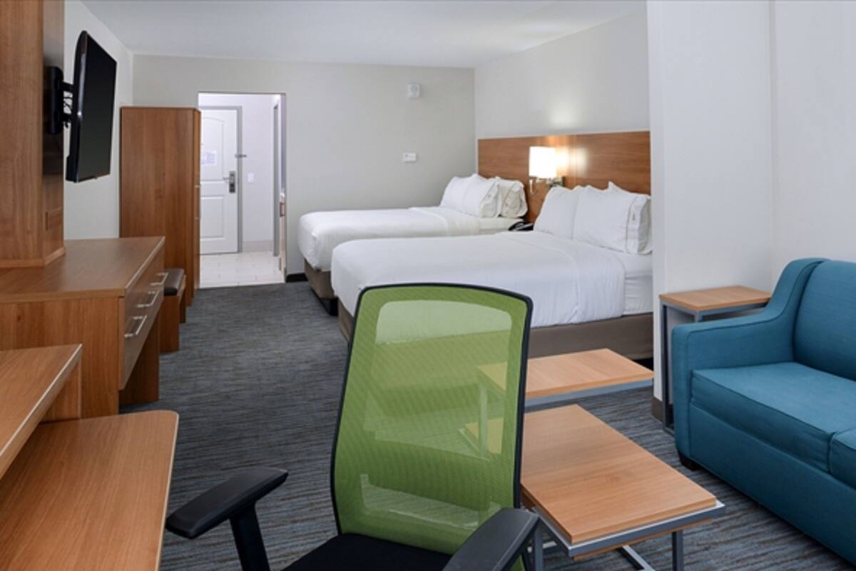 Una habitación de hotel con escritorio, dos camas, un sofá azul y un televisor en la pared.