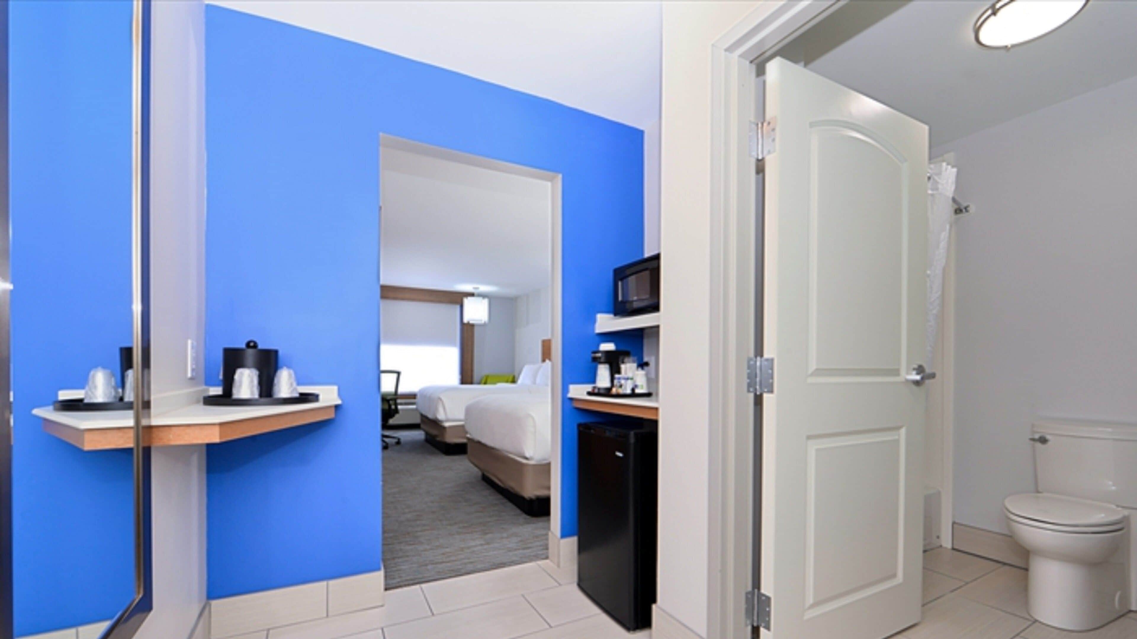 A hotel room with a bed, a desk, a microwave, and a toilet.