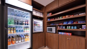 A kitchenette with a refrigerator stocked with beverages, a microwave, and shelves with snacks and toiletries. - Holiday Inn Express & Suites Lexington Midtown - I-75 by IHG (Lexington)