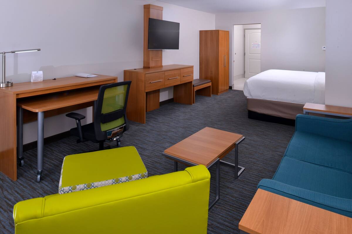 Una habitación de hotel con escritorio, televisión, armario, cama y dos sofás.