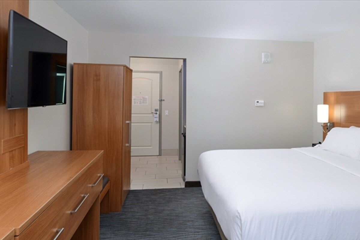 Een hotelkamer met een bed, een aan de muur bevestigde televisie, een houten dressoir en een deur naar een andere kamer.