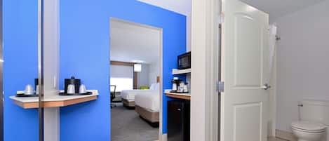 A hotel room with a blue accent wall, a bed, a desk with a computer, a microwave, and a small refrigerator.