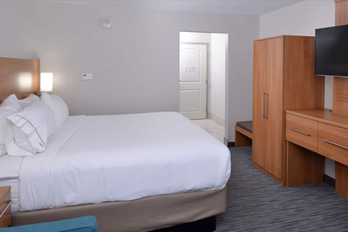 Una habitación de hotel con una cama, televisión, armario y escritorio.