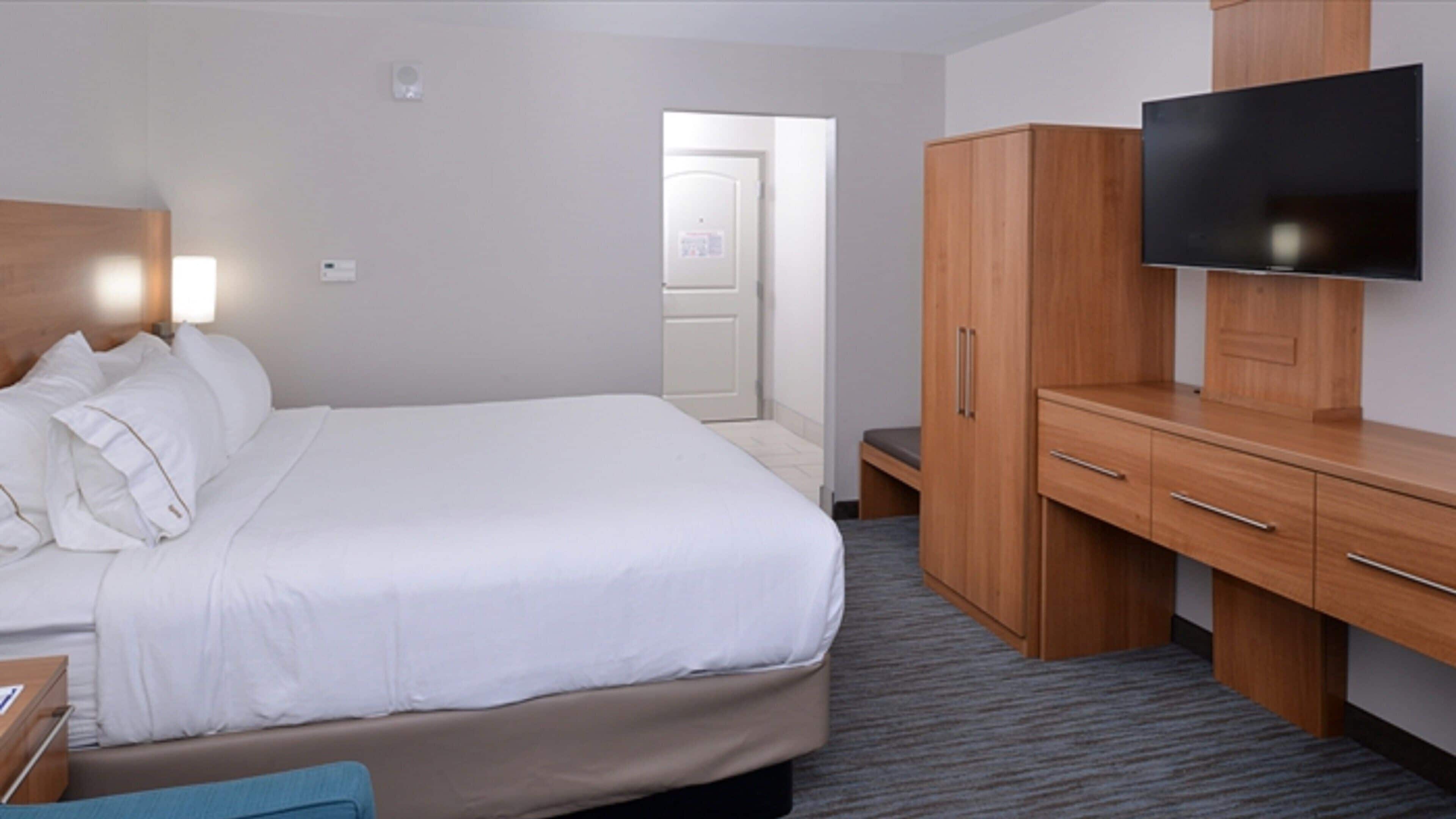 A hotel room with a bed, a TV mounted on the wall, a wardrobe, and a door leading to another room.