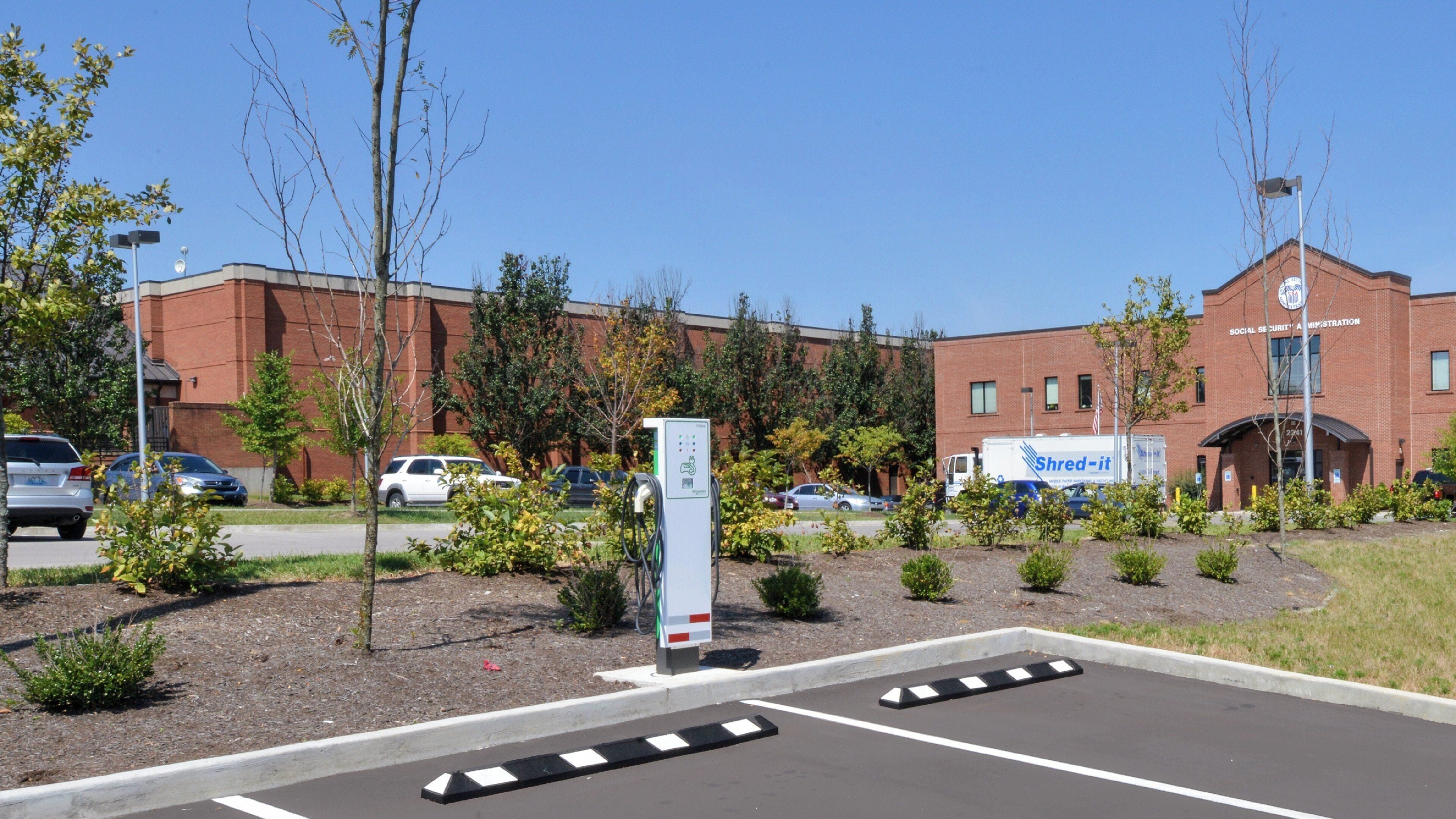 Een parkeerplaats met oplaadpunten voor elektrische voertuigen, een gebouw met de tekst 'Social Security Administration' en een vrachtwagen van 'Shred-it' voor leveringen.