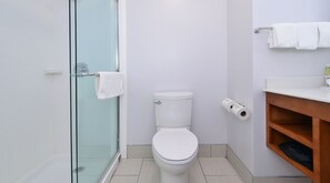 Een badkamer met een douchecabine van glas, een toilet en een houten wastafelmeubel met handdoekhouder.