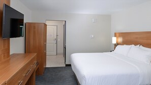 Een hotelkamer met een bed, een aan de muur bevestigde televisie, een houten dressoir en een deur die leidt naar een andere kamer.