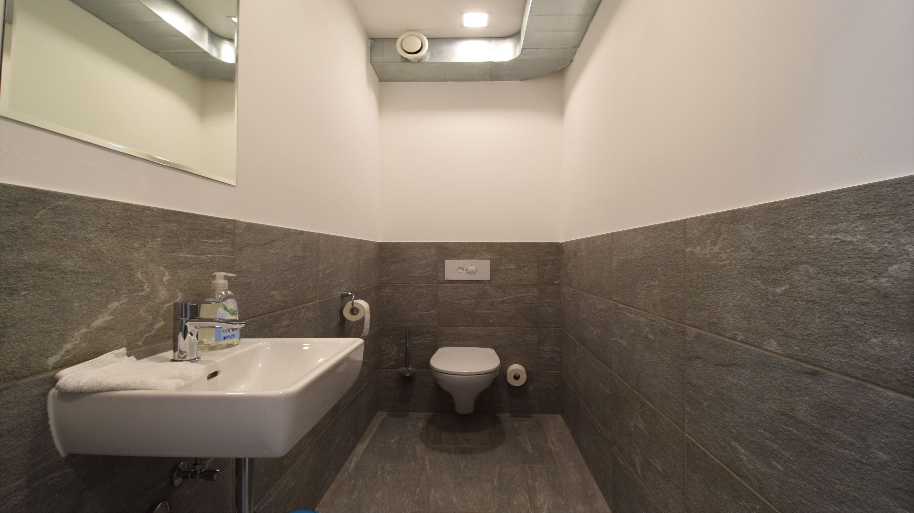 Une salle de bain avec un lavabo blanc, des toilettes et des murs recouverts de carreaux foncés.