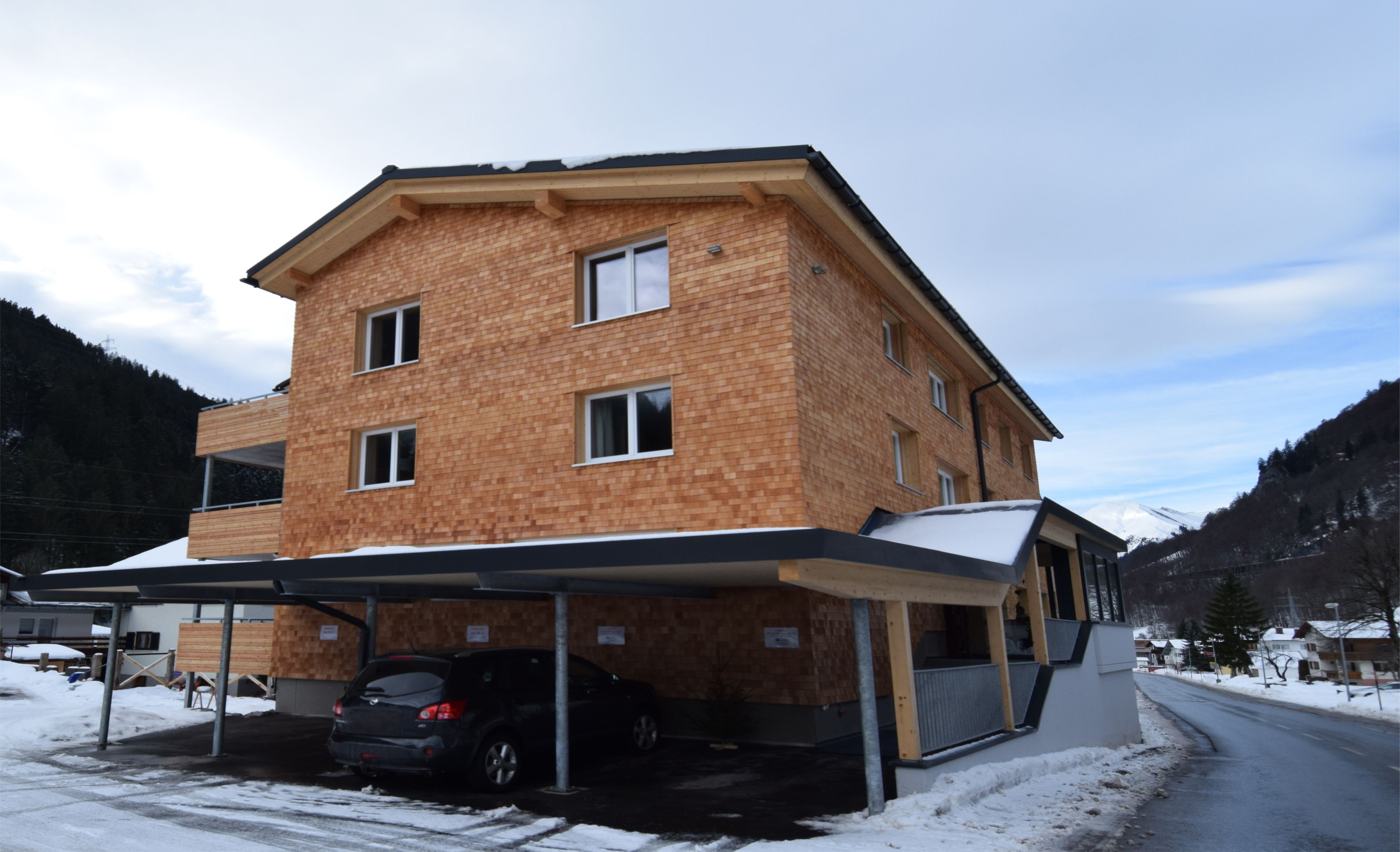 A multi-story building with a brick facade, a covered parking area, and a snow-covered landscape.