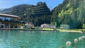 A clear lake with a rope buoy, a building with a red flag, and a mountain backdrop. - Alpine Lodge Klösterle am Arlberg (Klösterle am Arlberg)
