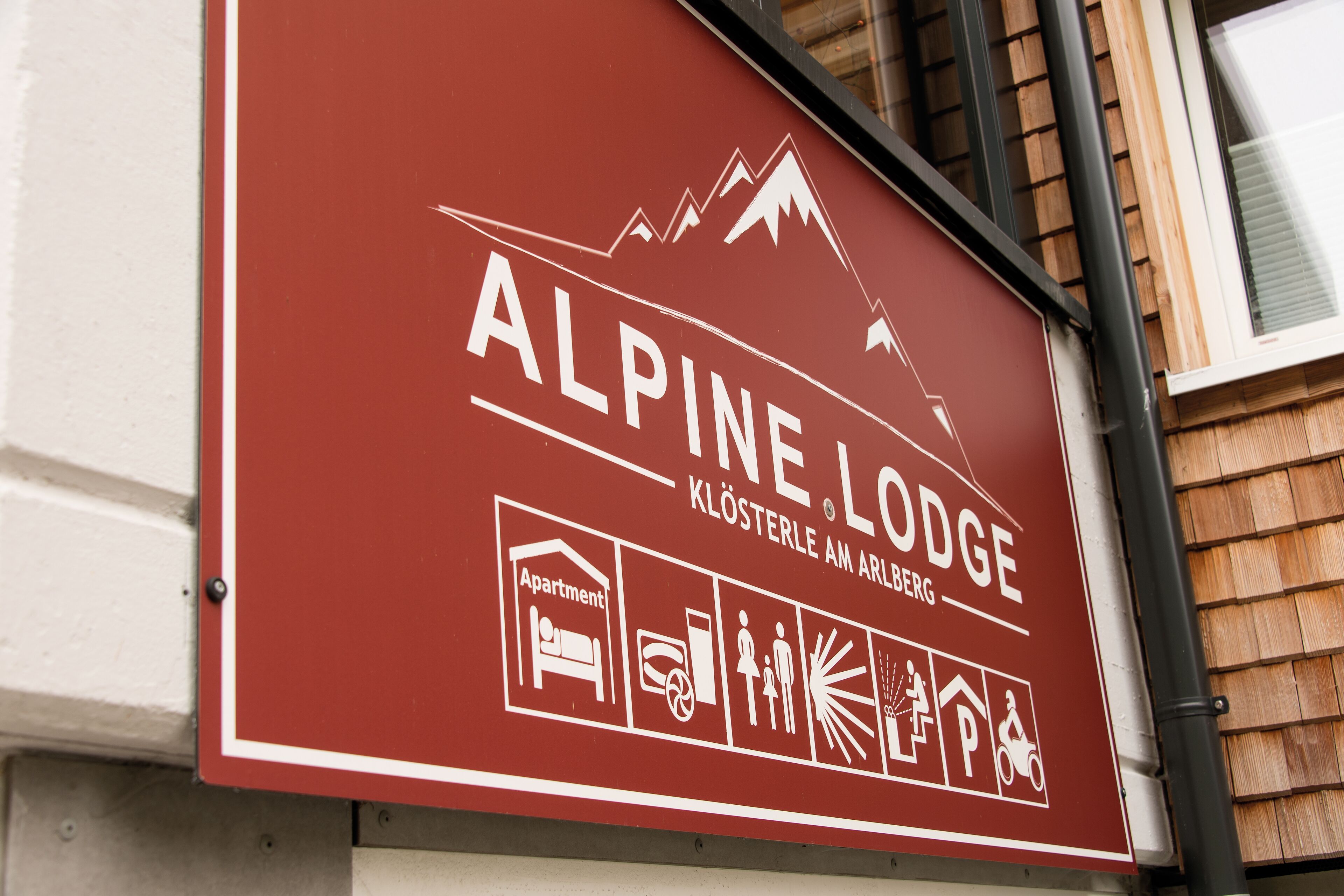 A sign for Alpine Lodge with icons indicating amenities like an apartment, parking, and a view of mountains.