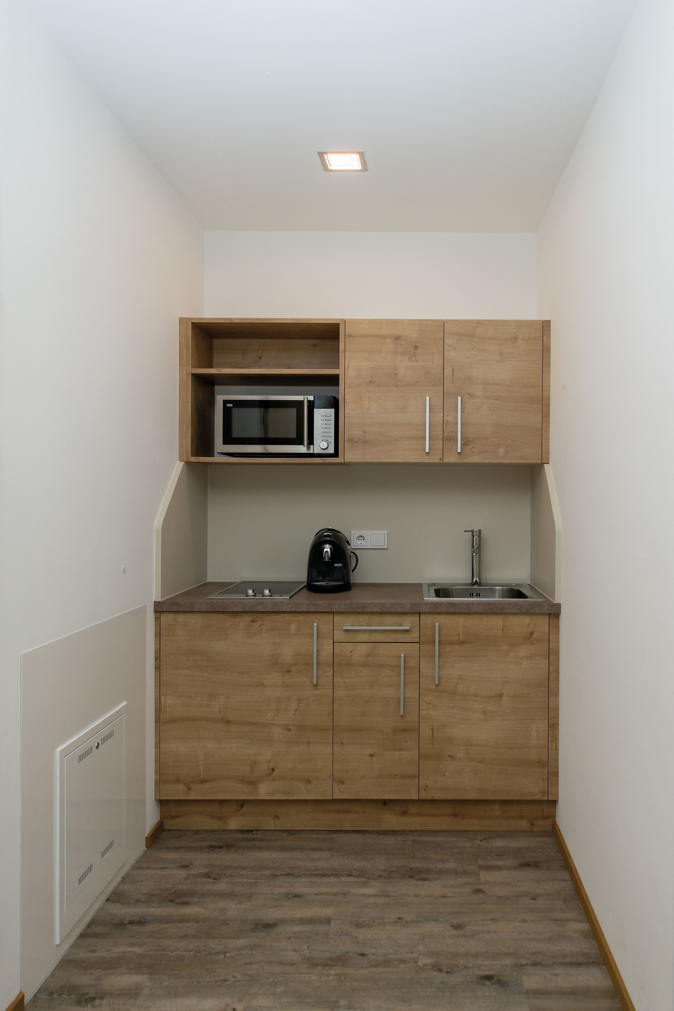 Une cuisine compacte avec des meubles en bois, un four à micro-ondes, une bouilloire et un évier.