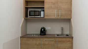 Une cuisine compacte avec des meubles en bois, un four à micro-ondes, une bouilloire et un évier.