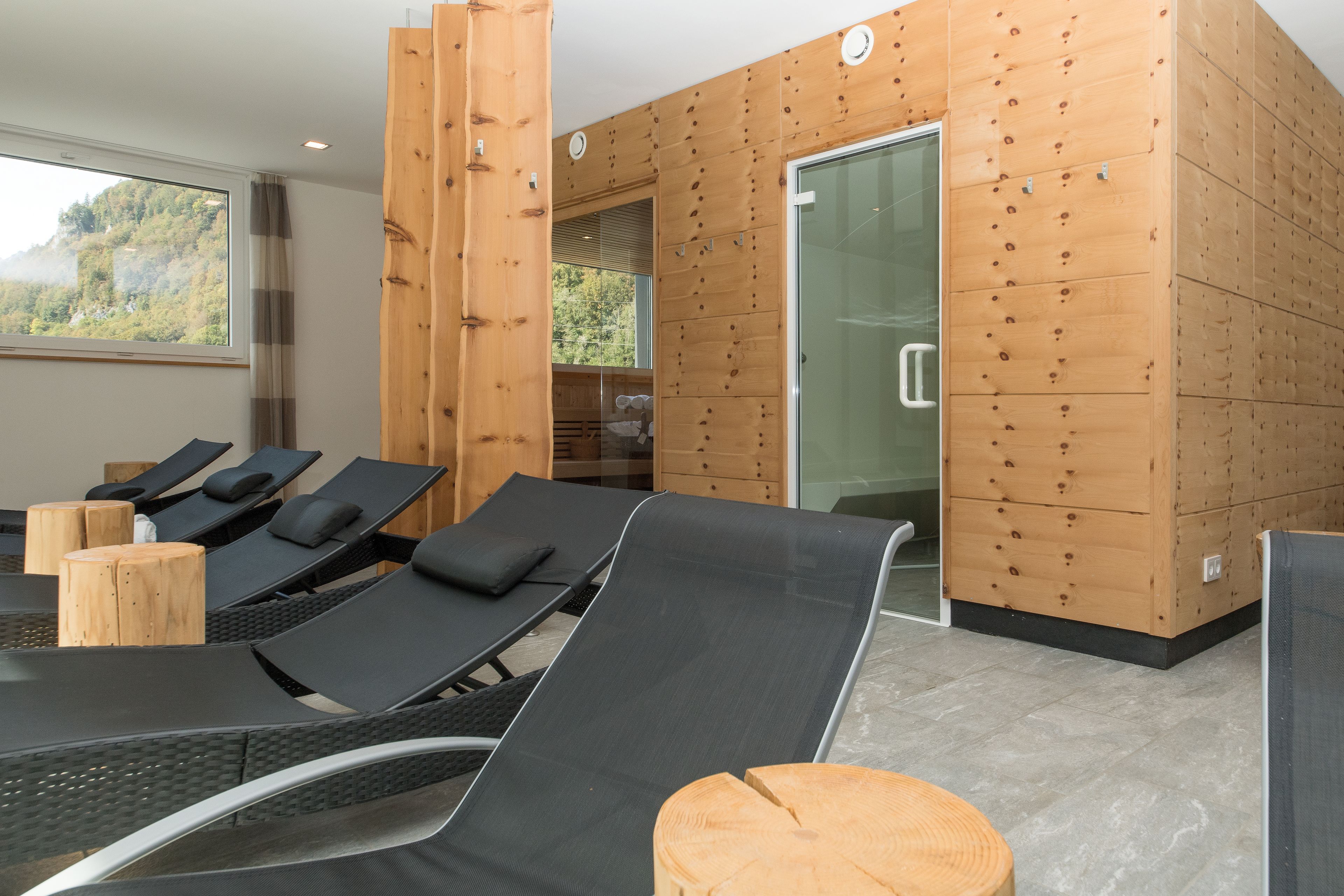 Un spa moderno con sillones de relax negros, detalles de madera y una puerta de vidrio que da a una zona de ducha.