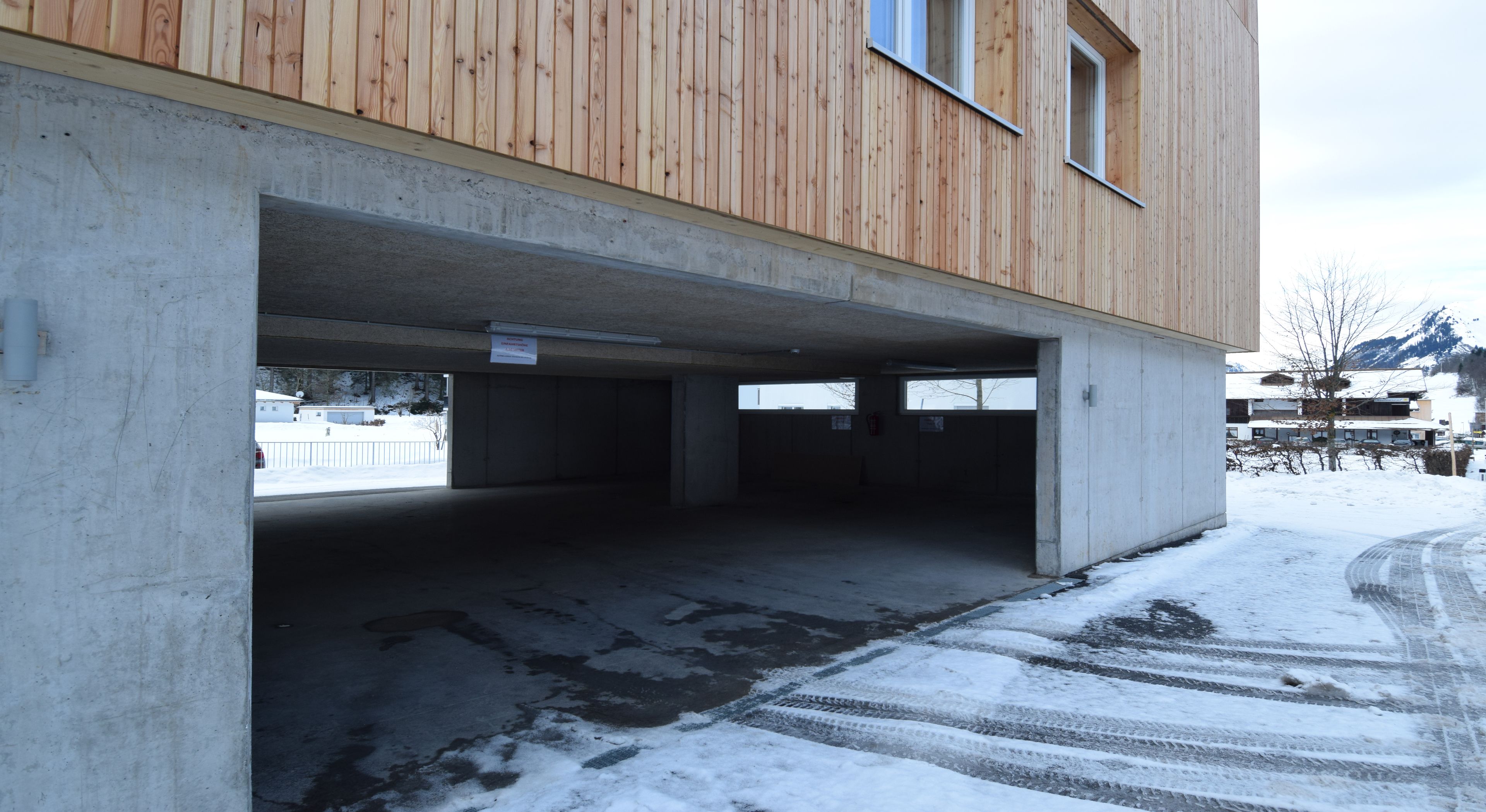 A building with a wooden exterior and a concrete structure underneath. There is a snow-covered ground and a clear sky.